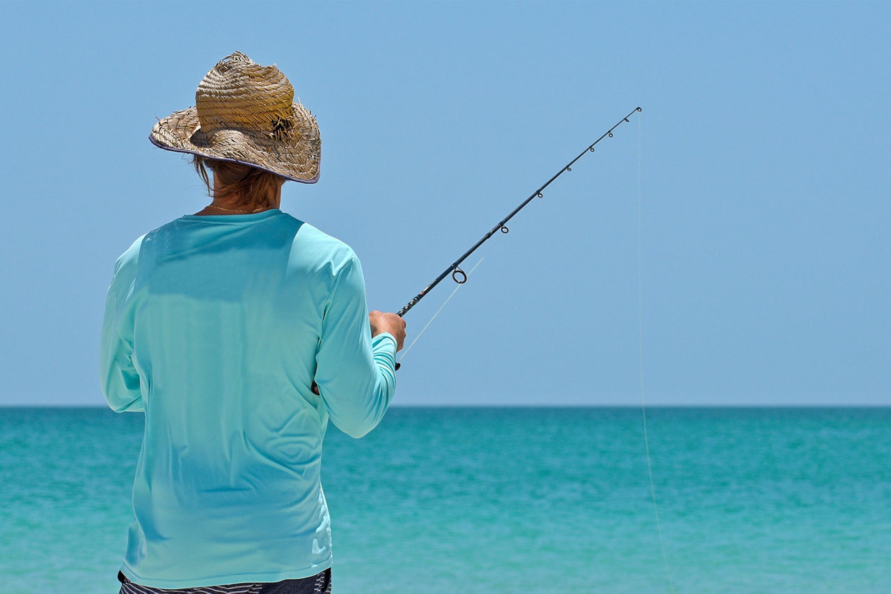 An unidentified local young man on the beach fishing in the shallow water of the Gulf